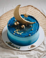 Blue cake with gold decorations on a white plate, featuring 'Eid' and 'Mubarak' text.