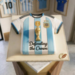 Cake designed like an Argentina soccer jersey with a trophy and text, placed on a stand.