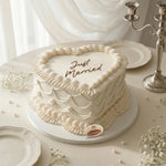 White wedding cake with 'Just Married' text on a decorative table.