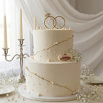 White wedding cake with gold accents and 'Gateau' branding, set against a white curtain background.
