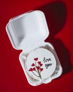 Round white compact mirror with floral design and 'love you' text in a white box on a red background