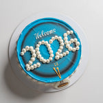 Cake with blue icing and white pearls spelling 'Welcome 2026' on a white background