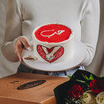 A person holding a heart-shaped cake with a red and white design, presumably for Valentine's Day.