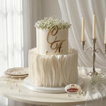 Two-tiered wedding cake with 'C A' initials and baby's breath on a white tablecloth.