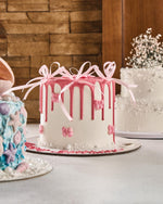 Decorative cake with pink drizzle and bows on a table with a wooden wall background