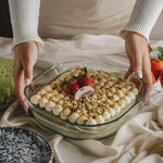 Glass dish with a layered dessert held by two hands on a light fabric background