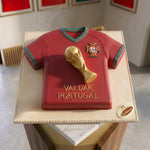 Red sports jersey cake with a gold trophy on a white plate, featuring the Portugal national team emblem.