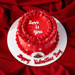 Red Valentine's Day cake with 'Love is you' text on a red fabric background