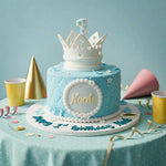 A light blue and white tiered birthday cake decorated with a white crown topper, a central white oval plaque reading 'Noah', and blue script text on the front, displayed on a table with party hats, cups, and confetti against a soft blue background.