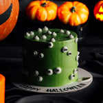 Green Halloween cake with eyeballs in front of pumpkins