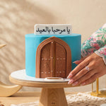 Decorative cake with a blue base and brown archway, held by a hand wearing a ring.