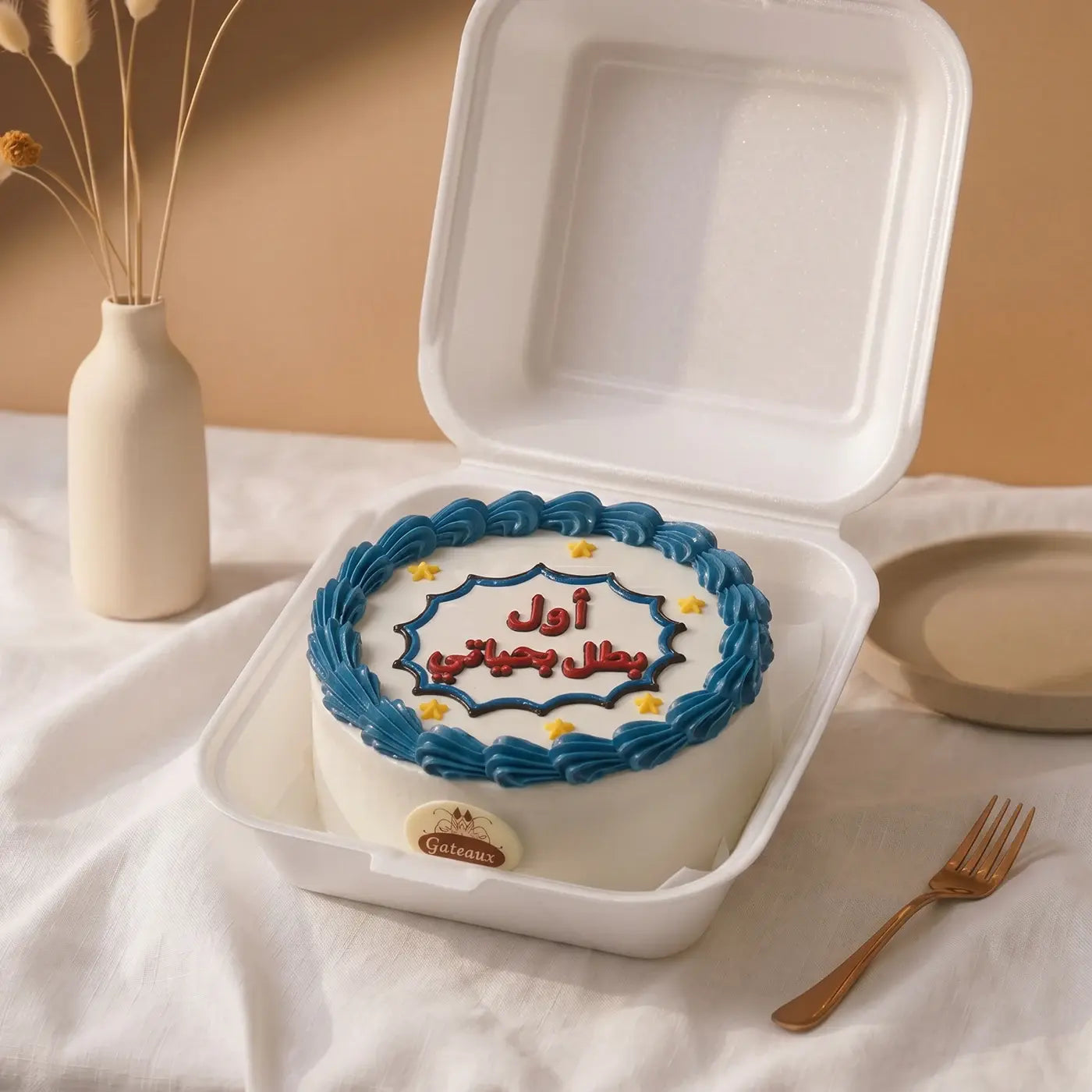 Decorative cake with blue icing in a white takeout container on a light surface.