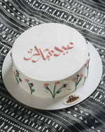 Decorative cake with floral designs and text on a patterned tablecloth