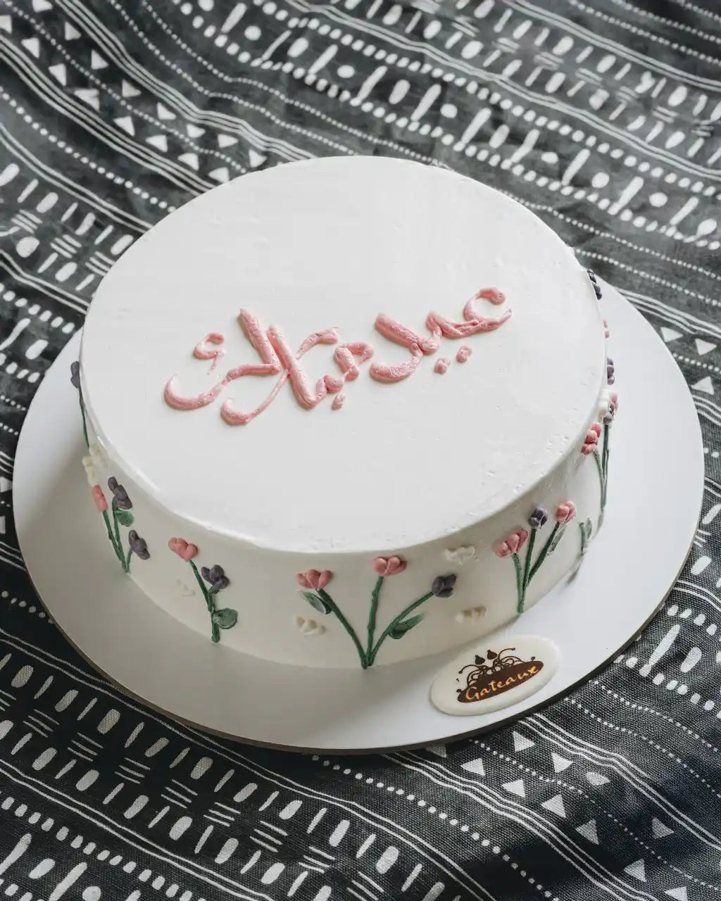 Decorative cake with floral designs and text on a patterned tablecloth