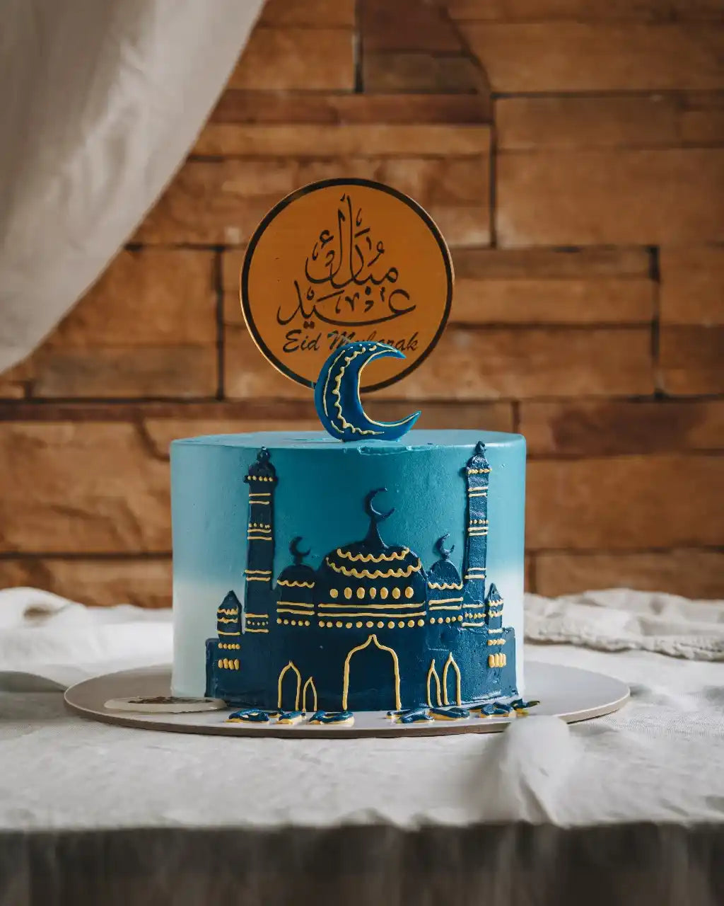 Blue cake with gold detailing and a crescent moon on top, set against a wooden wall.