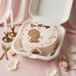 A round pink cake in a white foam box, decorated with two cartoon bear figures, small red hearts, and the text 'Over 365 days' on top. The cake is styled on a pink fabric surface with candles, forks, rose petals, and pink roses around it.