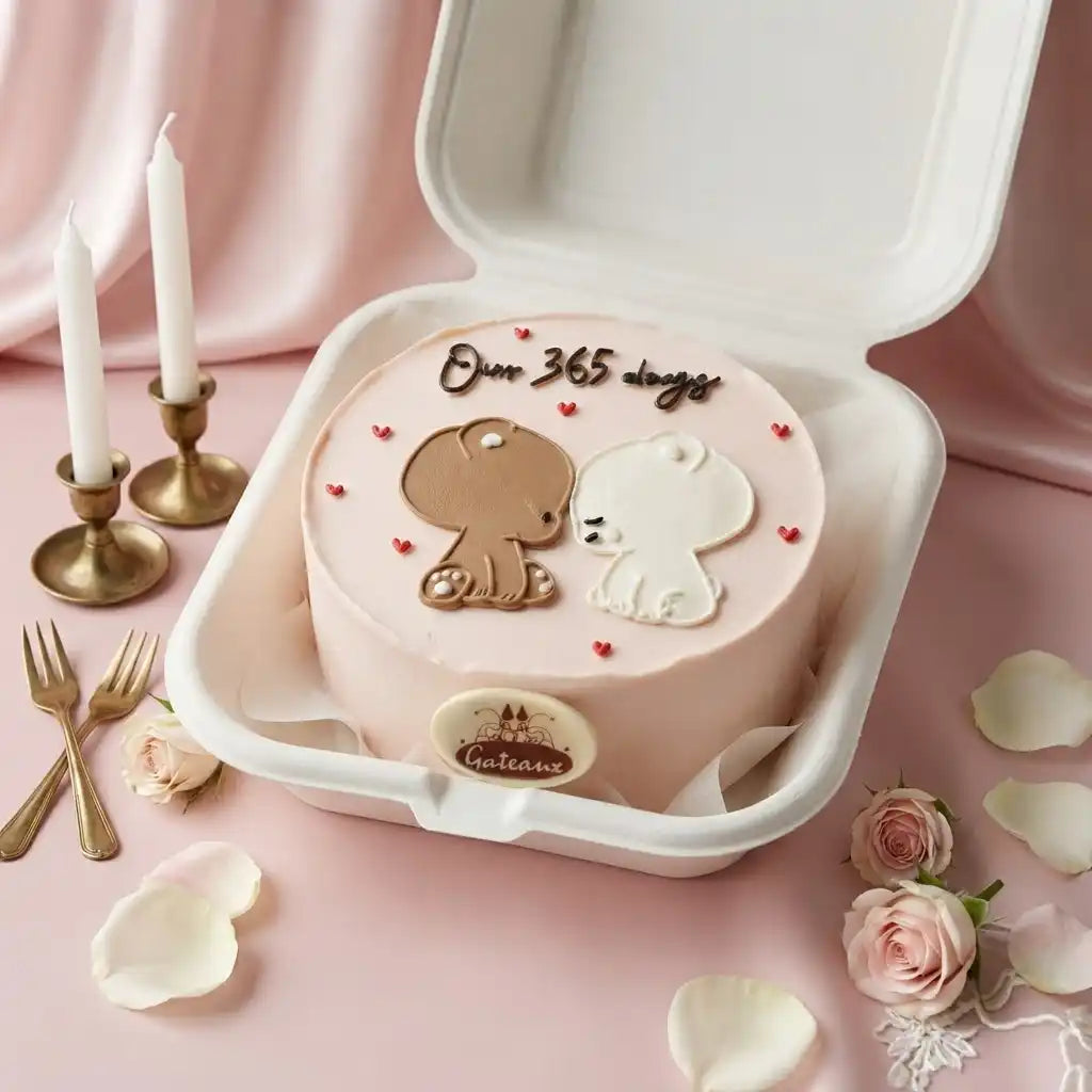 A round pink cake in a white foam box, decorated with two cartoon bear figures, small red hearts, and the text 'Over 365 days' on top. The cake is styled on a pink fabric surface with candles, forks, rose petals, and pink roses around it.
