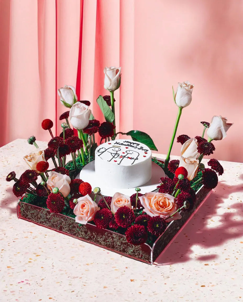 Decorative floral arrangement with a small cake on a pink background