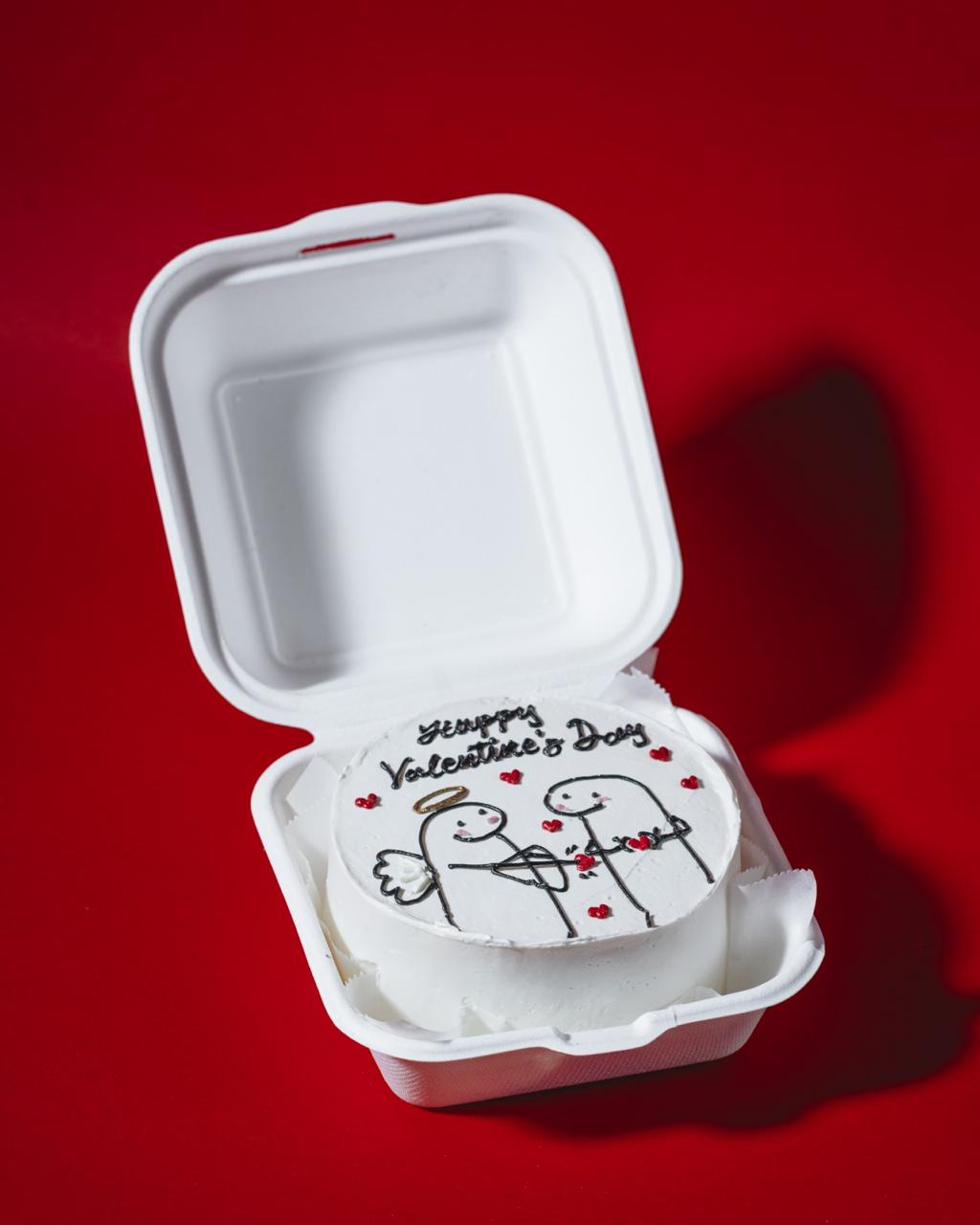 Small cake in a takeout container with 'Happy Valentine's Day' text on a red background