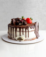 A decadent Black Forest cake with chocolate icing, decorated with cherries and a strawberry on top, presented on a plate.