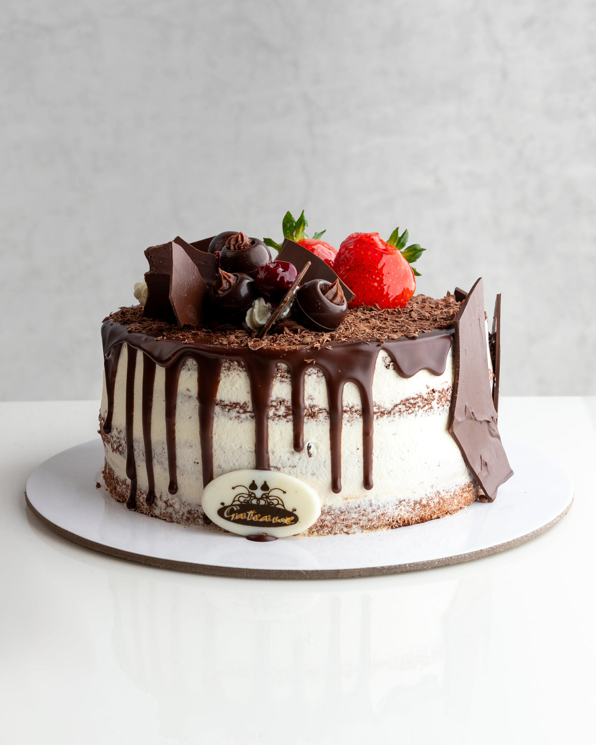 A decadent Black Forest cake with chocolate icing, decorated with cherries and a strawberry on top, presented on a plate.