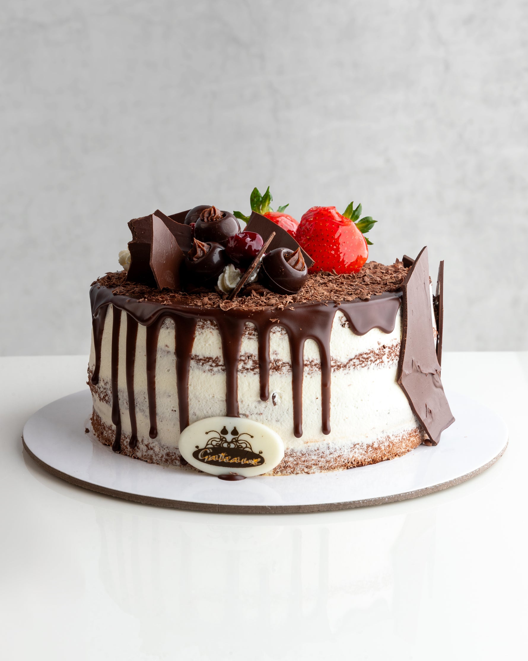 A decadent Black Forest cake with chocolate icing, decorated with cherries and a strawberry on top, presented on a plate.