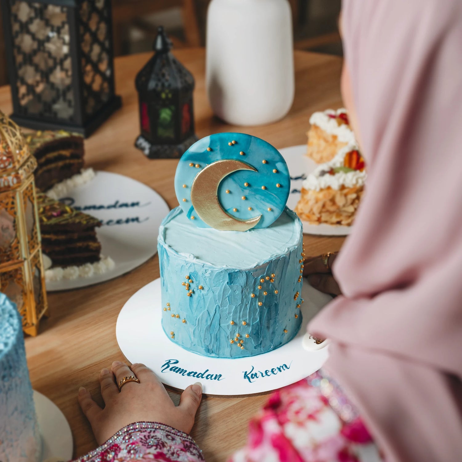 Blue cake with a moon decoration on a table with 'Ramadan Kareem' written on it.