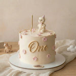 Children's birthday cake with a unicorn topper and 'One' candle on a neutral background