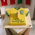 Cake designed like a yellow soccer jersey with a trophy and text, placed on a table.