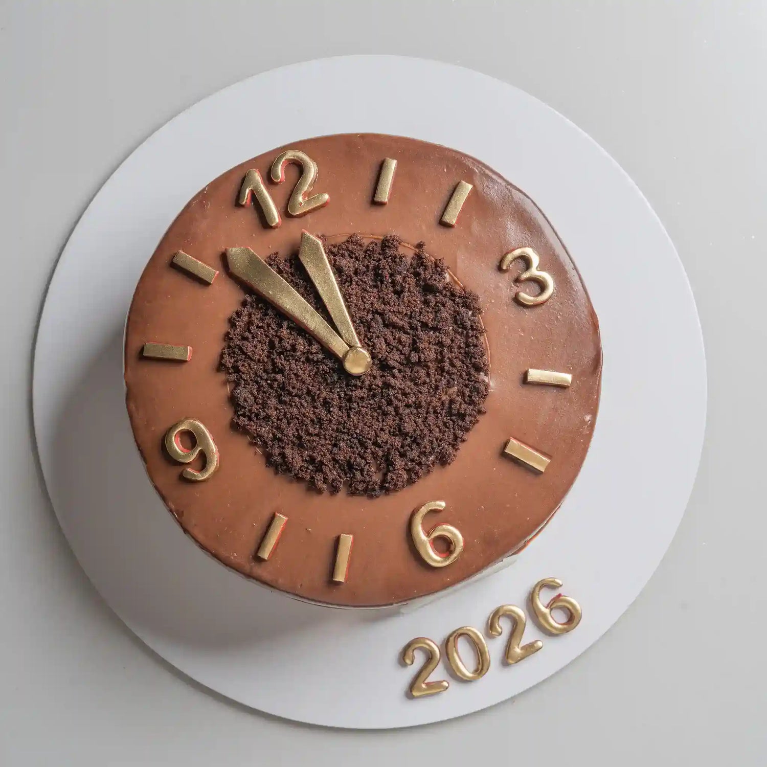 Chocolate cake designed like a clock with gold numbers and '2026' on a white background