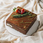 Square chocolate cake with green leaves and strawberries on a white plate