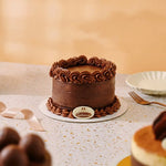 A chocolate cake with piped frosting rosettes on top and around the base, displayed on a white plate on a speckled countertop. A small round plaque in front reads Gauthier, and a fork and plate are visible nearby.