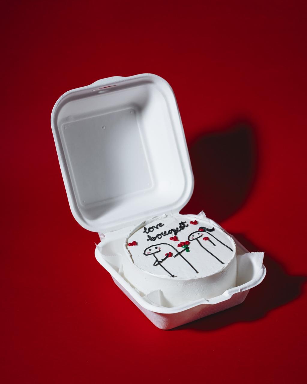 Small white cake with decorative elements in a takeout container on a red background