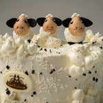 Cake with sheep figurines and white frosting, featuring a Gateau logo.