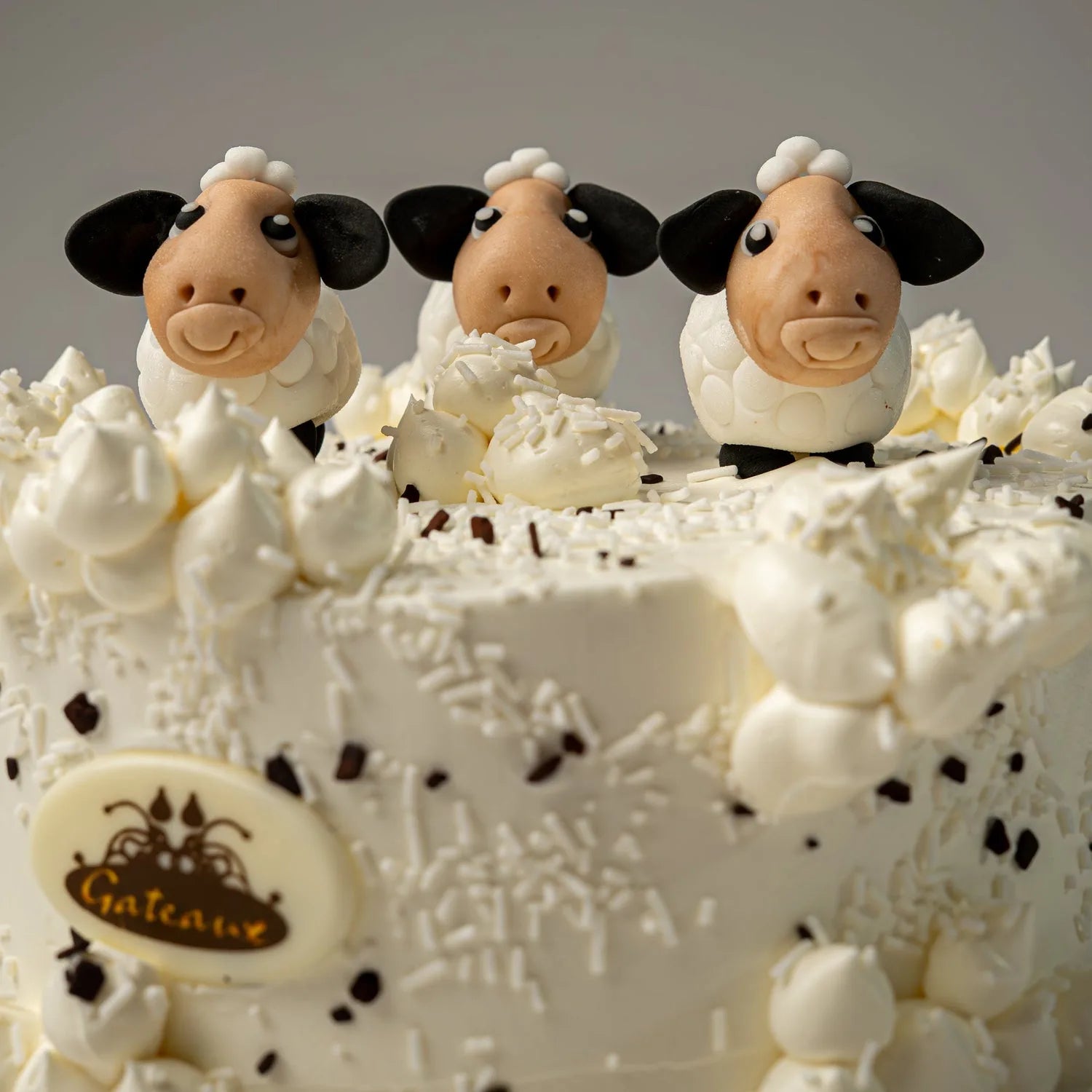 Cake with sheep figurines and white frosting, featuring a Gateau logo.