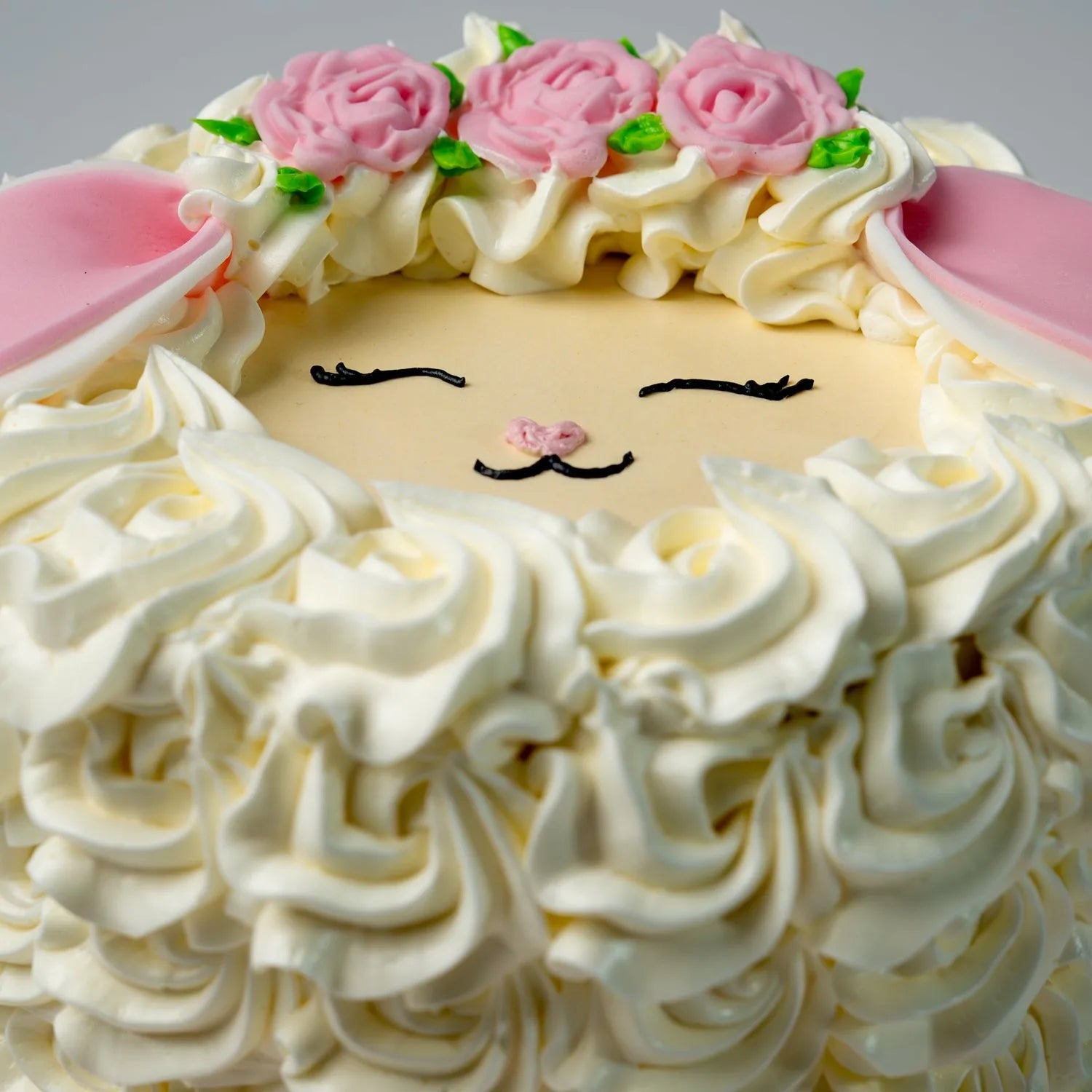 Sheep-shaped cake with white frosting, pink flowers, and a face design on a gray background