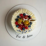 Decorative cake with fruits on a white plate with 'Eid Al Adha' text