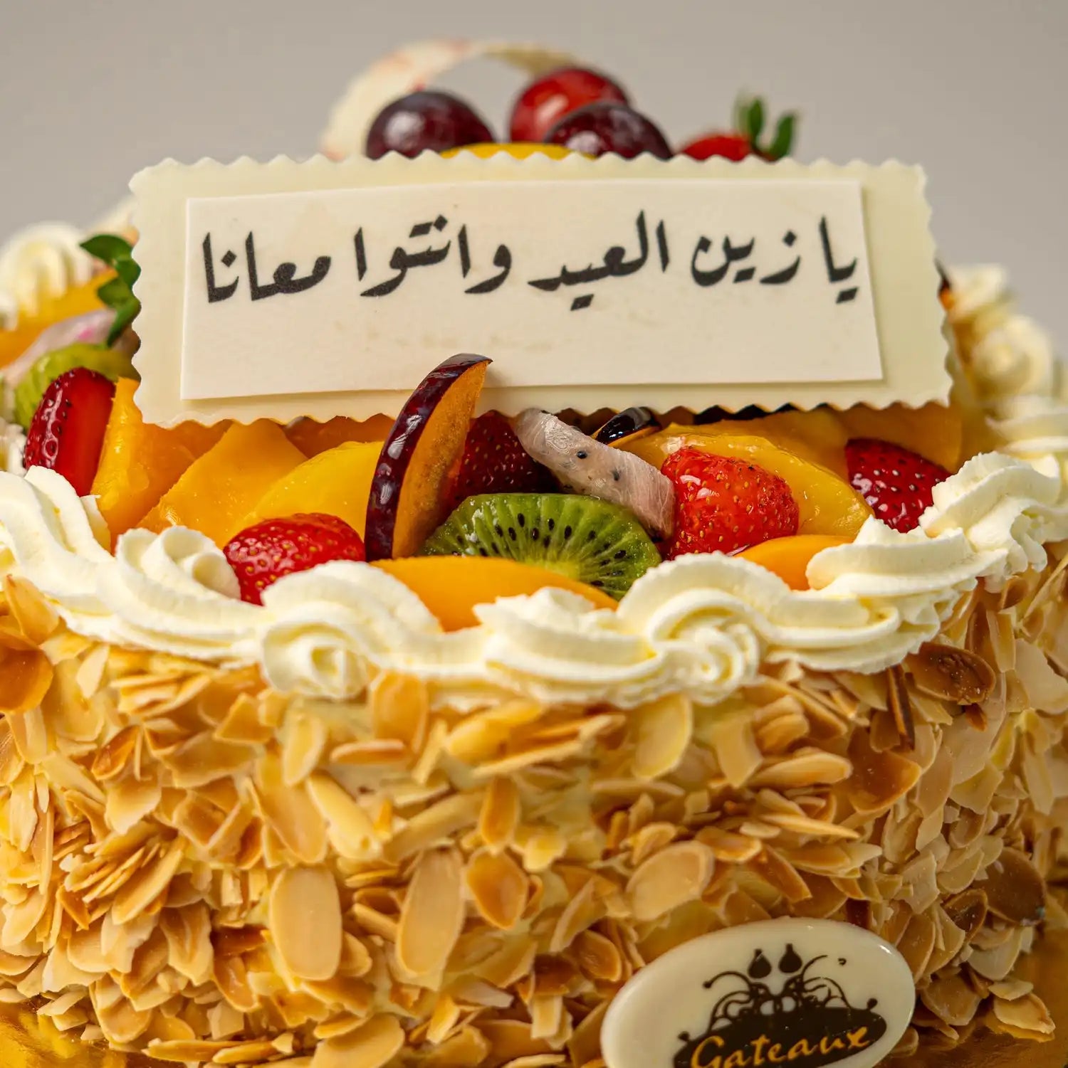 Decorative cake with fruits and a message in Arabic, featuring the brand 'Gâteaux'.