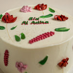 Decorative cake with floral designs and 'Ed Al Adha' text on a light background