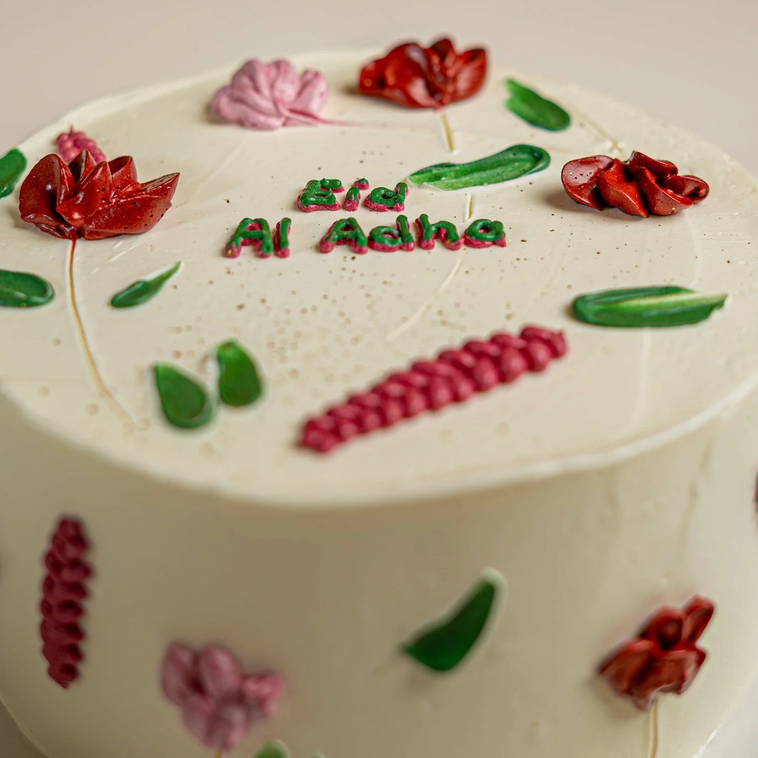 Decorative cake with floral designs and 'Ed Al Adha' text on a light background