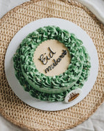 Green cake with 'Eid Mubarak' on a white plate on a woven mat
