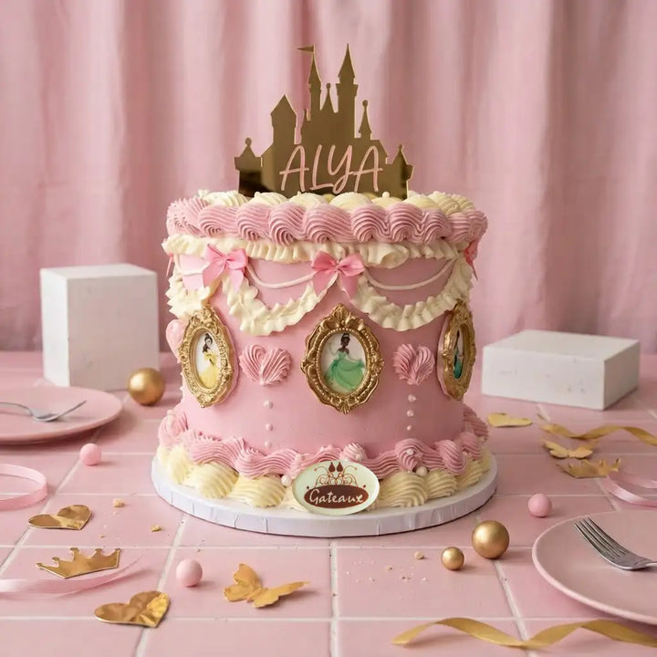 A pink and cream royal theme birthday cake decorated with piped frosting, pink bows, gold frames, and character illustrations, topped with a gold castle topper reading 'ALYA'.