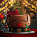 Decorative cake shaped like a reindeer with a Christmas tree and lights in the background