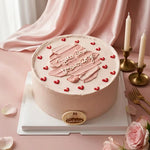 A round pink frosted cake on a white square board, decorated with red heart candies and piped pink lettering that reads 'You are my overcomer.' A small round cake topper with the brand name 'Galactus' is attached at the front.