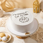 White cake with 'Happy Eid Al Adha' text on a decorative table.