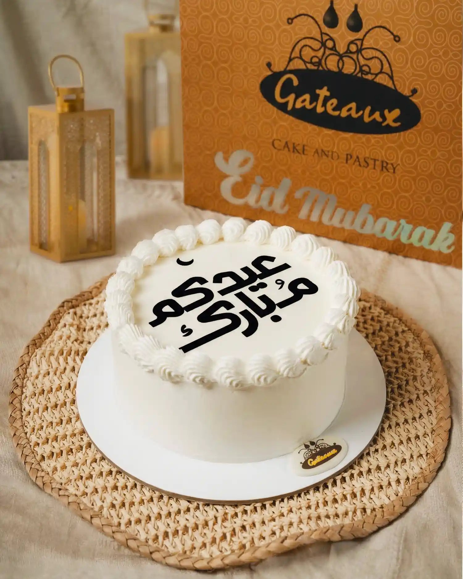 White cake with Arabic text on a woven mat, with 'Gateau' branding in the background.