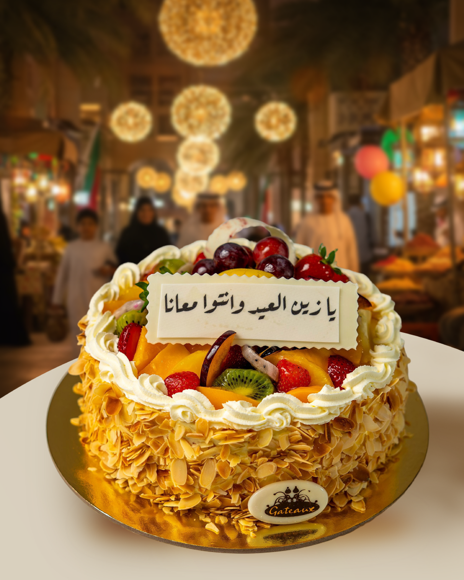 Decorative cake with fruit toppings on a gold plate, set against a blurred background of people and lights.