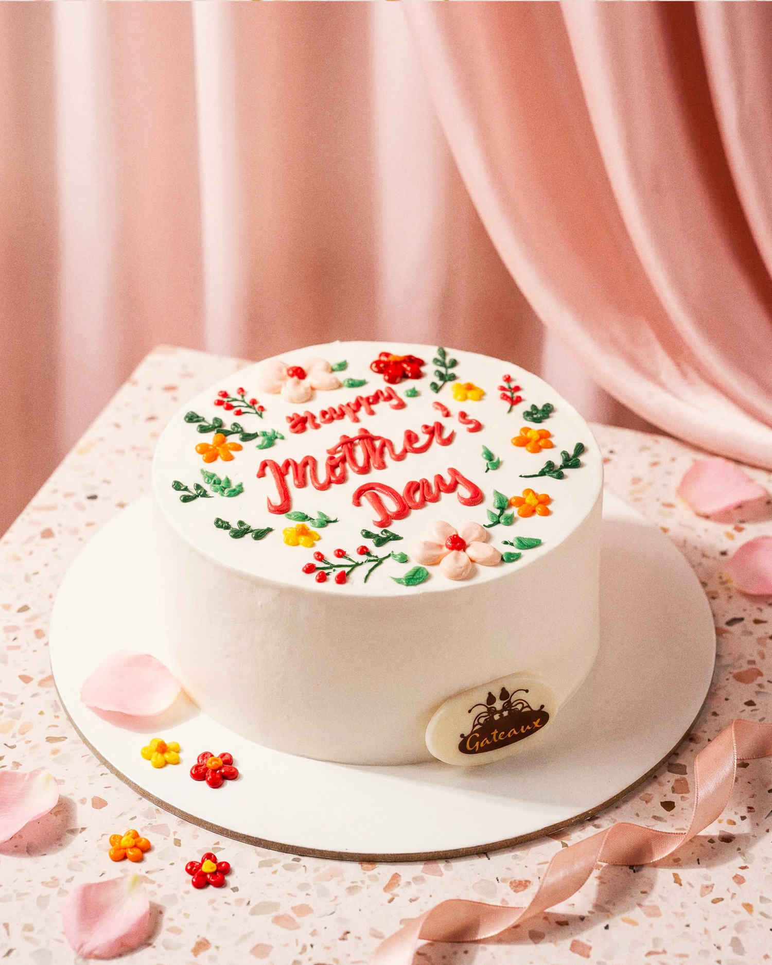 White cake with 'Happy Mother's Day' text and floral decorations on a pink background
