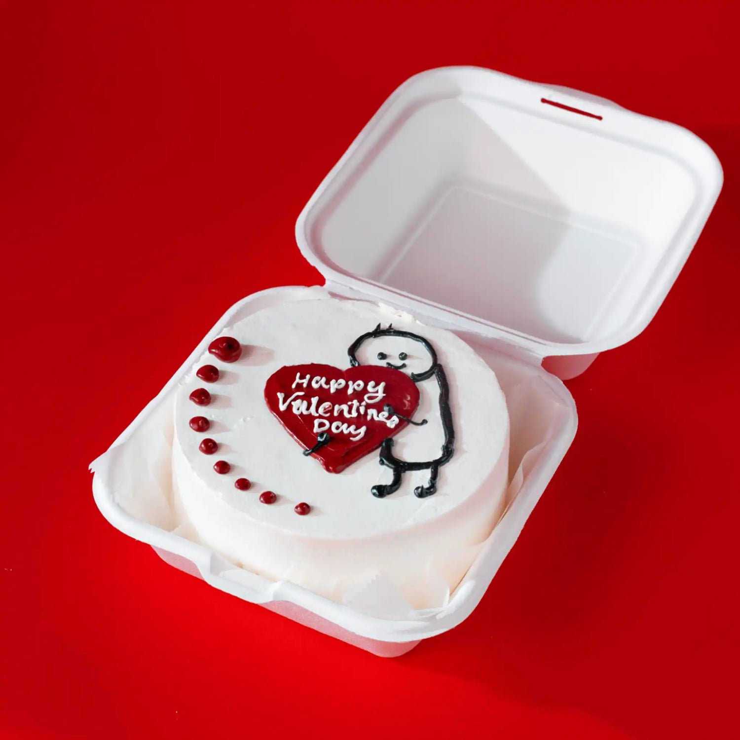 Small white cake with 'Happy Valentine's Day' decoration in a clear container on a red background