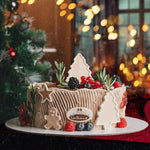 Decorative cake with Christmas-themed elements on a table with festive lights in the background